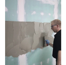 Mann trägt Fliesenkleber mit einer Kelle auf eine Wand auf.