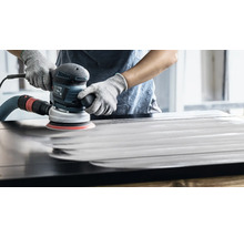 Eine Person schleift mit einem Exzenterschleifer eine Holzoberfläche.