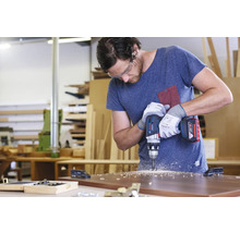 Ein Mann bohrt mit einer Akku-Bohrmaschine ein Loch in ein Holzbrett.