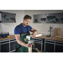 Mann arbeitet mit einer Einhandzwinge an einem Holzstück in einer Werkstatt.