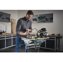 Ein Mann arbeitet mit einem Multifunktionswerkzeug an einem Werkstück auf einer Werkbank in einer Werkstatt.