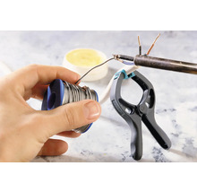 Lötzinnrolle in der Hand, Lötarbeiten an einem Kabel mit einer Klemme fixiert