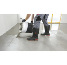 Estrich gießen: Mann schüttet Estrich aus Eimer auf Boden.