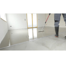 Ein Mann verteilt Ausgleichsmasse auf einem Boden mit einem Rakel.