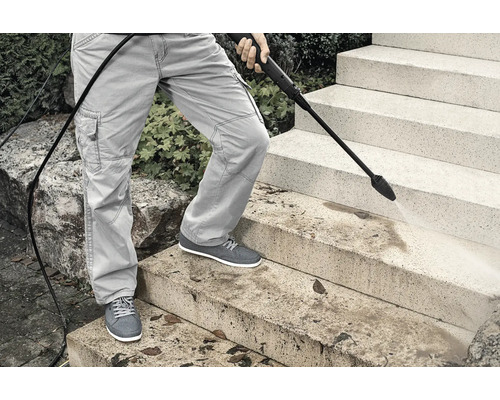 Eine Person reinigt Steintreppen mit einem Hochdruckreiniger.