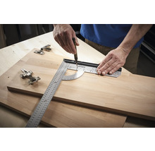 Eine Person verwendet ein Winkelmessgerät und einen Stift, um Markierungen auf einem Holzbrett neben Scharnieren zu machen.