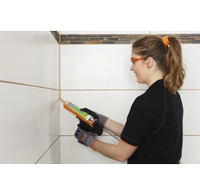 Frau dichtet Fugen zwischen Fliesen mit Silikon ab.