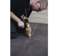 Handwerker, der mit einer Fugenpistole Fugenmasse zwischen Fliesen aufträgt.