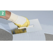 Eine Hand mit Schutzhandschuh verteilt Fliesenkleber mit einer Zahnspachtel.