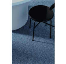 Detailaufnahme eines blauen Teppichs mit einem runden, weißen Tisch und einem schwarzen Hocker.