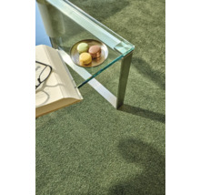 Detailansicht eines Zimmers mit einem grünen Teppich, einem Tisch mit Macarons, einem Buch und einer Brille.