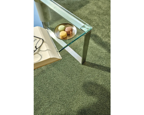 Detailansicht eines Zimmers mit einem grünen Teppich, einem Tisch mit Macarons, einem Buch und einer Brille.