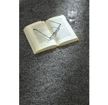 Ein Buch, eine Brille und ein Glas Wasser liegen auf einem grauen Teppich.