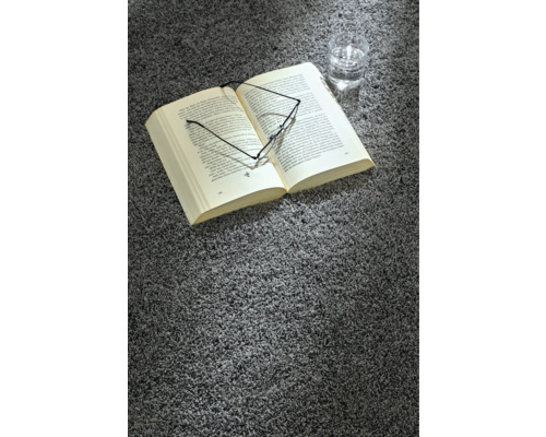 Ein Buch, eine Brille und ein Glas Wasser liegen auf einem grauen Teppich.