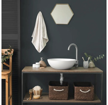Modernes Badezimmer mit weißem Aufsatzwaschbecken auf einem Holzunterschrank, hoher silberner Armatur und hexagonalem Spiegel vor dunkler Wand.