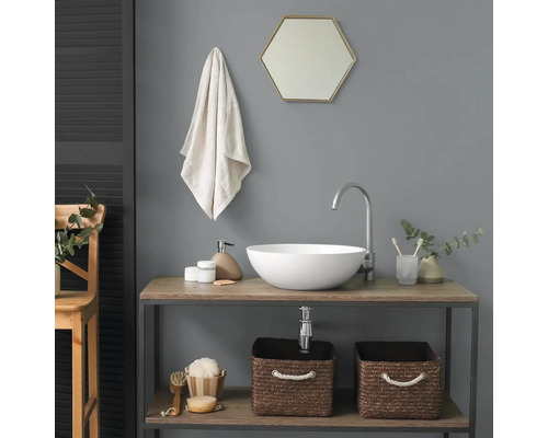 Modernes Badezimmer mit weißem Aufsatzwaschbecken auf einem Holzunterschrank, hohem Wasserhahn, sechseckigem Spiegel und geflochtenen Körben.