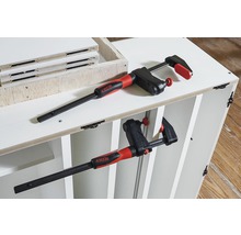 Zwei Schraubzwingen fixieren ein weißes Möbelstück.