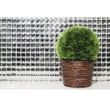 Dekorative grüne Kunstpflanze im braunen Topf vor einer Mosaikwand