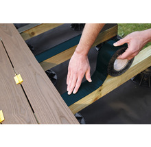 Eine Person befestigt ein Dichtungsband auf einem hölzernen Unterbau für eine Terrasse.