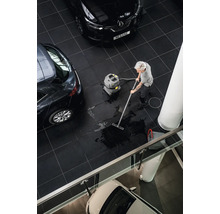 Eine Person reinigt einen Fliesenboden mit einem Nass Trockensauger in einem Ausstellungsraum mit Autos.