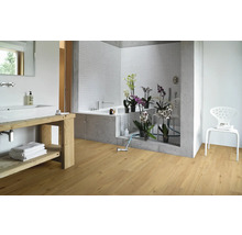 Helles Badezimmer mit Holzboden, Waschbecken mit Holzunterschrank, Badewanne und weißem Stuhl.