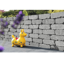 Gestapelte Mauersteine bilden eine Gartenmauer mit einem Spielzeugpferd davor.