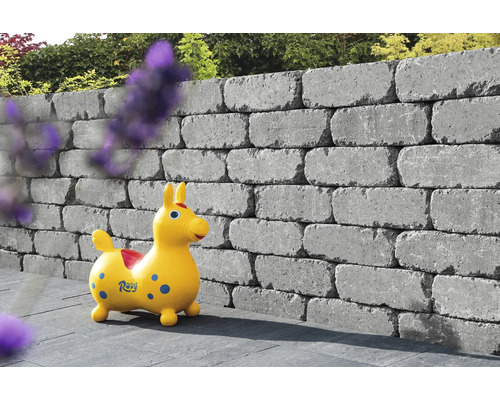 Gestapelte Mauersteine bilden eine Gartenmauer mit einem Spielzeugpferd davor.