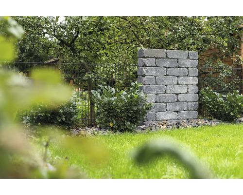 Landschaftsbild mit Mauerwerk aus Steinblöcken und Metallzaun im Garten