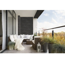 Balkon mit Rattansofa, Kissen, Decke, Laternen und Ziergräsern in Töpfen.