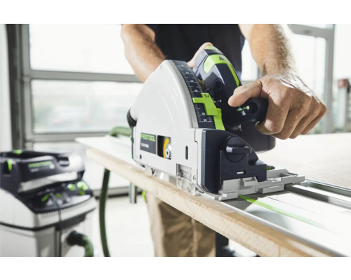 Mann sägt Holzbrett mit einer Festool Tauchsäge auf einer Führungsschiene, mit einem Staubsauger im Hintergrund
