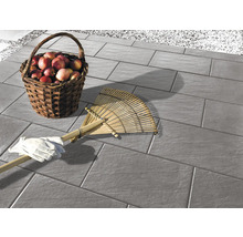 Pflastersteine auf einer Terrasse mit einem Korb voller Äpfel, einem Rechen und Gartenhandschuhen