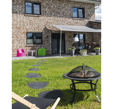 Außenbereich mit Feuerstelle, Liegestuhl, Wegplatten und Beschattung vor einem Wohnhaus