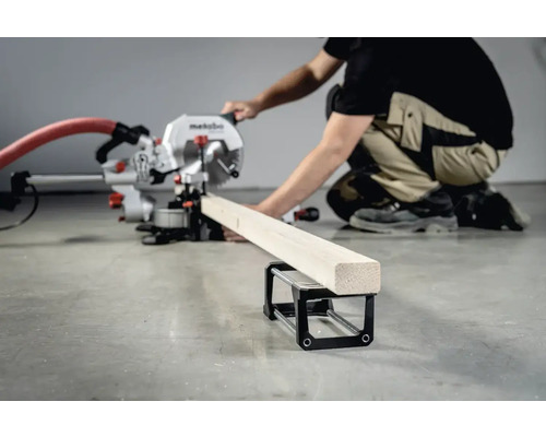 Eine Person bedient eine Kappsäge zum Zuschneiden eines Holzstücks, das auf einem Werkstückauflagebock liegt.