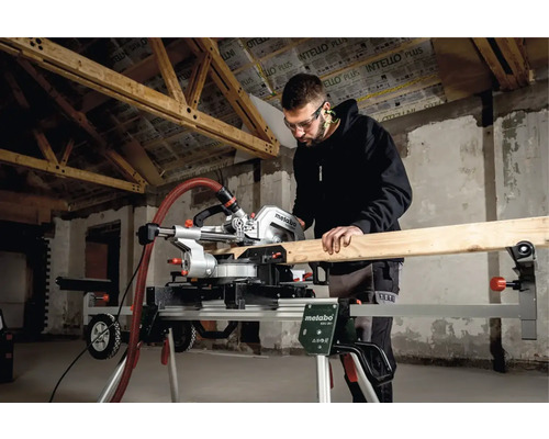 Mann mit Schutzbrille sägt Holz mit einer Metabo Kappsäge auf einem Untergestell in einem Rohbau.