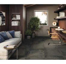 Wohnzimmer mit Sofa, Schreibtisch und dunklen Bodenfliesen.