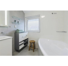 Helles Badezimmer mit Badewanne, Waschtisch, Unterschrank, Handtüchern, Holzschemel und Fenster mit Jalousie