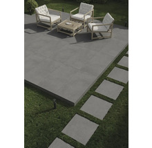 Terrasse mit grauen Fliesen, Sitzgruppe mit Holzrahmen und weißen Polstern sowie Trittplatten im Rasen.