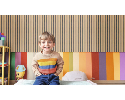 Ein Kind sitzt vor einer Wand mit Holzpaneelen und farbigen Flächen