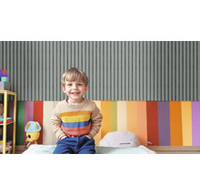 Ein lächelnder Junge sitzt in einem Kinderzimmer mit gestreifter Tapete und farbenfroher Wandgestaltung.