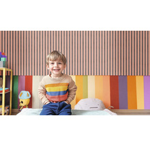 Ein Kind steht vor einer Wand mit vertikalen Streifen in einem Kinderzimmer.