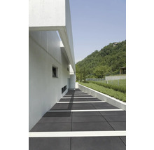 Außenbereich mit grauen Bodenplatten, einem weißen Gebäude und einer grünen Hügellandschaft