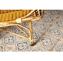 Detailansicht von Bodenfliesen mit floralem Muster unter einem Korbsessel