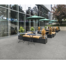 Außenbereich mit grauen Bodenfliesen, Tischen, Bänken und Sonnenschirmen.