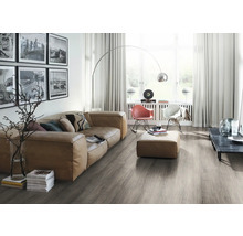 Heller Wohnraum mit Sofa, Sesseln, Stehlampe und grauem Holzboden