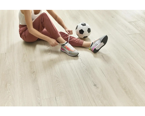 Frau sitzt auf hellem Holzboden und bindet ihre Sportschuhe, daneben ein Fußball