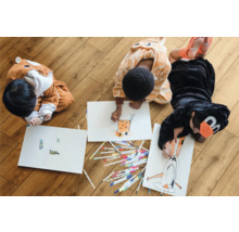 Drei Kinder in Tierkostümen malen auf dem Boden mit Stiften auf Papier.