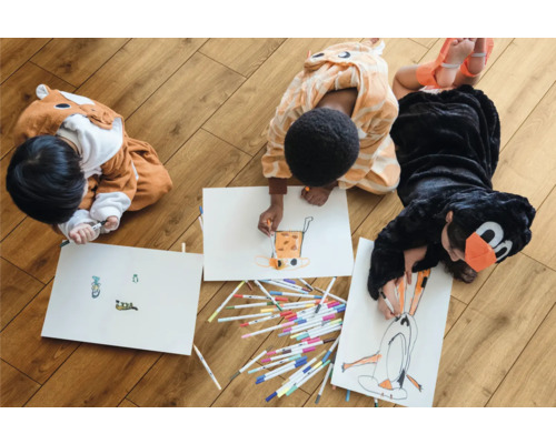 Drei Kinder in Tierkostümen malen auf dem Boden mit Stiften auf Papier.