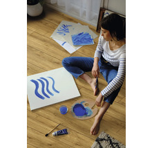 Eine Frau sitzt auf einem Laminatboden und malt mit blauer Farbe.