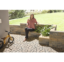Gartenbereich mit Bodenplatten in Natursteinoptik, Mauer und einer Frau, die auf einer Bank sitzt