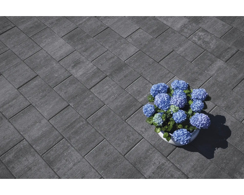 Graue Pflastersteine im Fischgrätmuster mit blauen Hortensien im Topf.